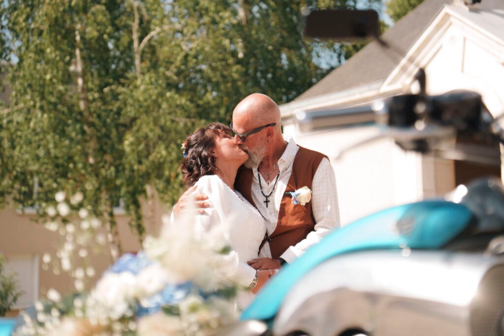 Au premier plan une moto floutée avec un bouquet de mariage et des mariés en arrière plan | Photographe de mariage à Bourges