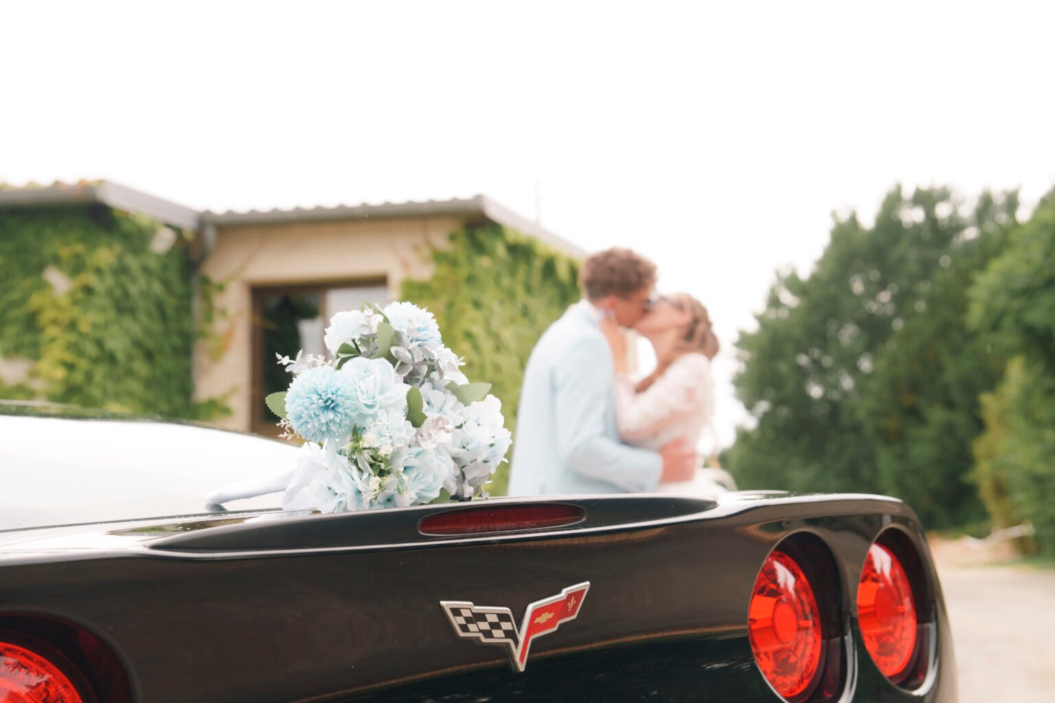Un couple de mariés en arrière plan et un bouquet et une corvette en premier plan