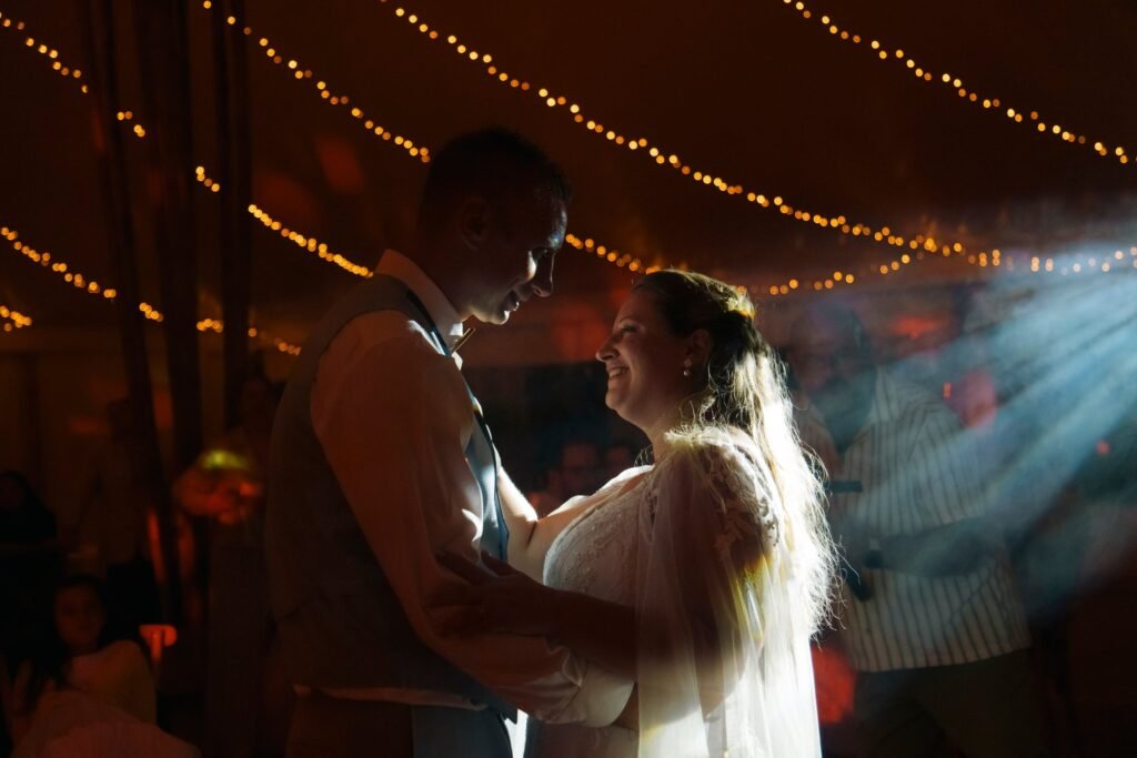 Les mariés dansent leur ouverture de bal sous les guirlandes lumineuses du chapiteau