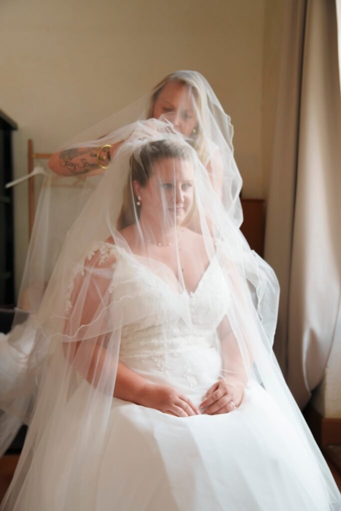 La mariée assise sous son voile, pendant qu'on le met en place