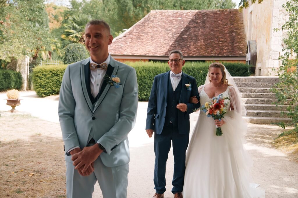 Le marié sourit en attendant, la mariée et son père approchent derrière lui
