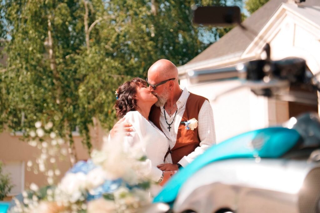 Au premier plan une moto floutée avec un bouquet de mariage et des mariés en arrière plan | Photographe de mariage à Bourges